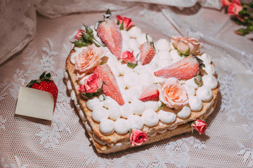 White cream sponge cake in the shape of a heart with roses and strawberries. Template for a note.  Close-up