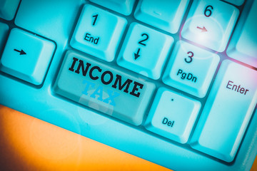 Conceptual hand writing showing Income Tax. Concept meaning Annual charge levied on both earned and unearned income White pc keyboard with note paper above the white background