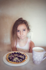 Drowsy and disheveled girl eating breakfast blueberry cake on plate and coffee in cup in the morning sitting at the table