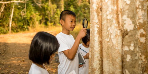 Kids children concept, boy and gril kids learning and journey outdoor in forest on hills, child holding book and pencil writing data from learning, holding magnifying glass for looking small insects