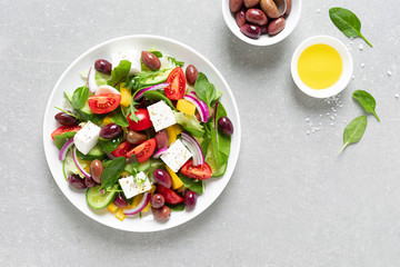 Greek salad with greens, olives and feta chesse on a white plate, top view