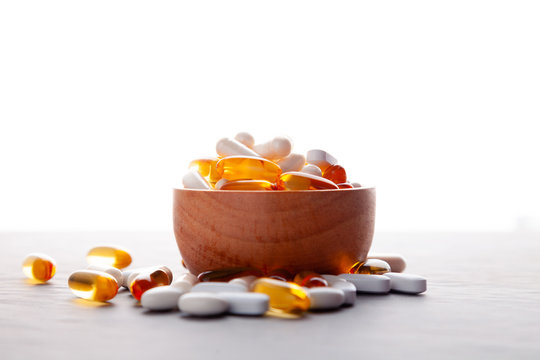 Assortment scattered pharmaceutical medicine vitamins, pills, drugs in wooden bowl on gray background. White food dietary supplement hard shell capsules filled with powder, fish oil softgel Omega 3