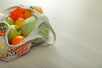 Net bag with vegetables and fruits on wooden table. Space for text