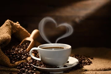 Photo sur Plexiglas Best-sellers dans la cuisine Tasse de café avec de la fumée en forme de coeur et des grains de café sur un sac de jute sur fond de bois ancien