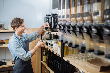 Sustainable shopping at small local businesses. Close-up image of man owner pours granola in paper bag from dispensers in plastic free grocery store. Seller workong in zero waste shop.