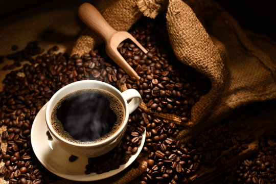 Cup of coffee with smoke and coffee beans on burlap sack