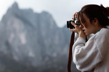 Side view of woman traveler in casual plaid shirt taking photo from opened window of nature at Dolomites mountains, Italy