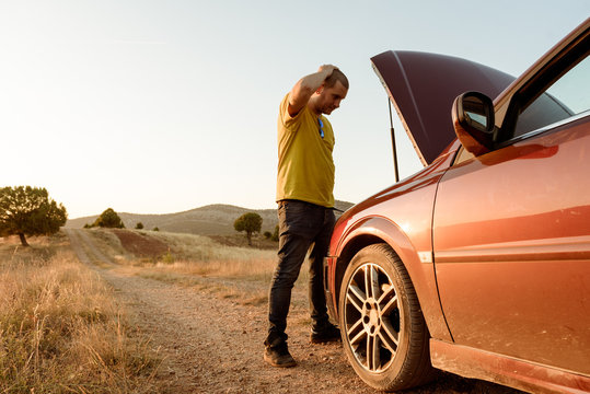 Man examining broken car in countryside