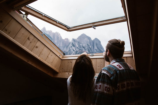 From below back view of faceless male and female travelers in casual clothing admiring landscape of Dolomites mountains at Italy from skylight