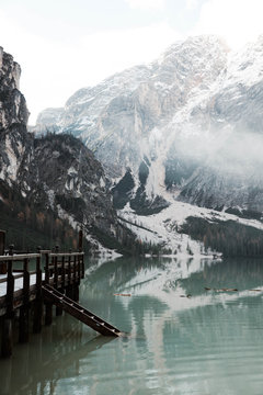 Wooden bridge pier on stilts on nebulous lake with reflection of powerful Dolomites mountains at Italy