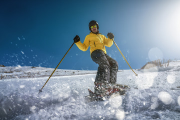 Full body young man in yellow outwear and sunglasses riding skis on snowy mountain slope on sunny winter day on resort