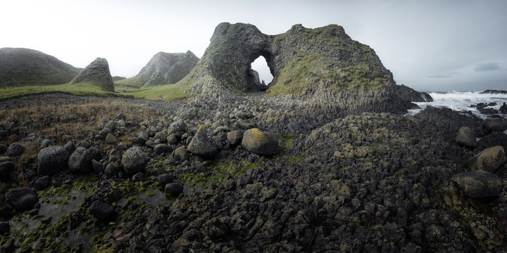 Side view of female in warm outfit standing on cliff edge within cave in harbour of Northern Ireland looking away into sea