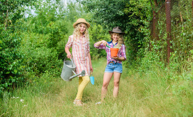 Naklejka na ściany i meble Kids having fun at farm. Eco farming concept. Planting and watering. Rustic children nature background. Agriculture concept. Girls in hats planting plants. Sisters helping at farm. Family farm
