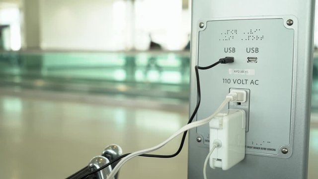 Young woman trying to plug in device at charging station at airport