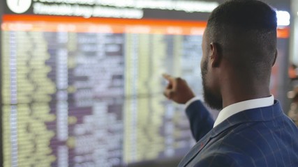 African businessman checking his flight boarding time at information board in airport terminal