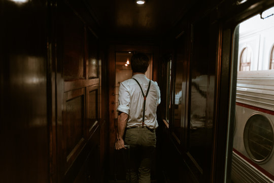 Back View Of Anonymous Man In Vintage Clothes Pulling Luggage And Walking In Hallway Of Old Train