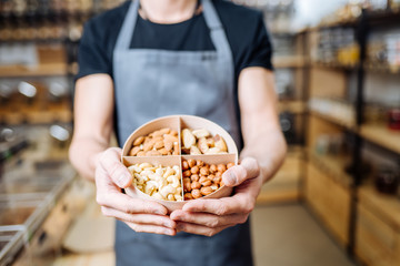 Man Owner selling different types of nuts in Zero Waste Shop. Lots of Healthy Food in Glass Bottles on Stand in Grocery Store. No plastic Conscious Minimalism Vegan Lifestyle Concept. Selective focus