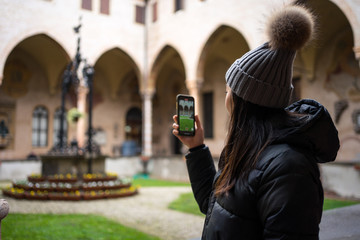 Side view of Asian female tourist in warm clothing and hat taking picture on mobile phone while exploring ancient Basilica of San Antonio at Padova at Italy