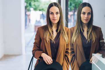 Confident long haired female buyer in stylish classy outfit standing next to shop window and looking at camera at mall