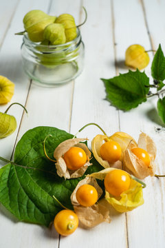 Physalis fruit (Physalis peruviana) also called uchuva, cape gooseberry or gold berries, native of Peru, on a wooden white board with leaves.