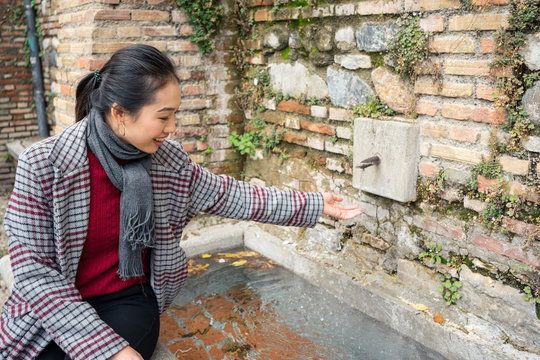 Young lady in casual clothing washing hands in street fountain