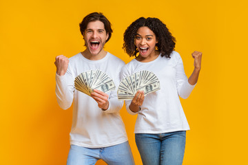 Overjoyed interracial couple holding lot of dollar cash, celebrating success together