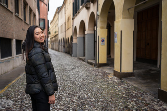 Female traveler in warm clothing walking on block stone road among historical beautiful buildings at Padova at Italy looking at camera