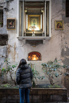 Back view of anonymous female looking at weathered wall and window with icons while standing on street outside old church