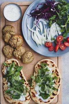 From above of food composition falafel and fresh vegetables on bread near with salad on cutting board