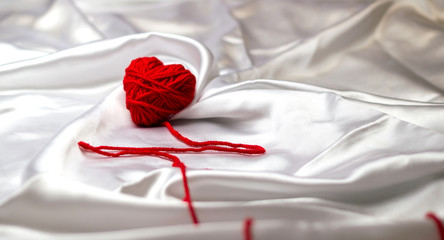 white silk fabric with bends and a red knitted heart with a pulse line for Valentine's Day, copy space. bot view