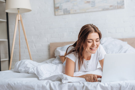happy young woman using laptop while chilling in bedroom