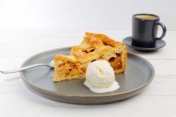 Piece of an apple pie with ice cream and cup of coffee espresso on white wooden table. Shallow focus.
