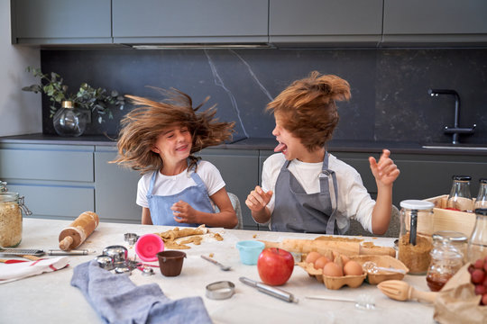Little male and female kids in aprons shacking heads laughing at modern kitchen while making cookies