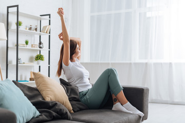 selective focus of young dreamy woman with outstretched hand relaxing in living room