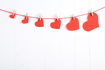 Red paper hearts hanging on white wooden background