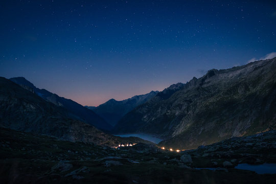 Mountain range and river between slopes with burning lights above in Switzerland
