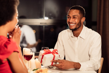African American Man Giving Gift To Surprised Woman In Restaurant