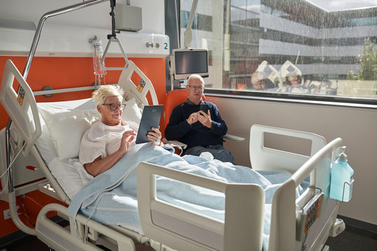 Senior couple using devices in hospital ward