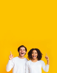 Interracial couple pointing upwards at copy space and looking at camera