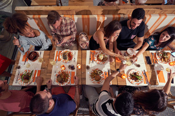From above of multiethnic male and female friends in casual clothing communicating and smiling while sitting at festive table at restaurant