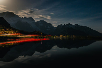 Dramatic breathtaking landscape of red-lit shore and dark tranquil water reflecting cloudy sky and mountains in evening in Switzerland