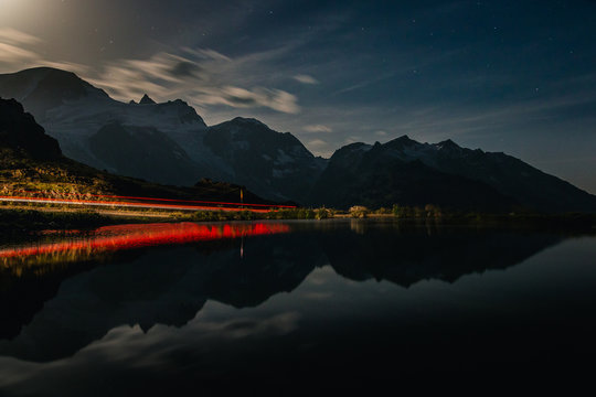 Dramatic breathtaking landscape of red-lit shore and dark tranquil water reflecting cloudy sky and mountains in evening in Switzerland