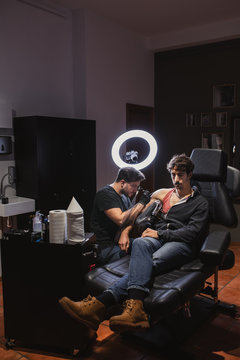 Master doing tattoo on forearm of male customer