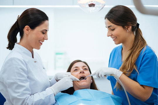 Dentist and assistant examining mouth of patient in chair with tools