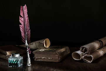Quill pen and a rolled papyrus sheet on a wooden table with old books