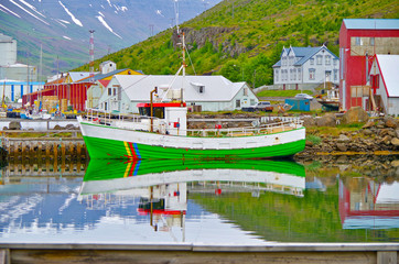 Colorful fishing boats and surrounding scenery and landscape reflect in even surface of lake or bay...