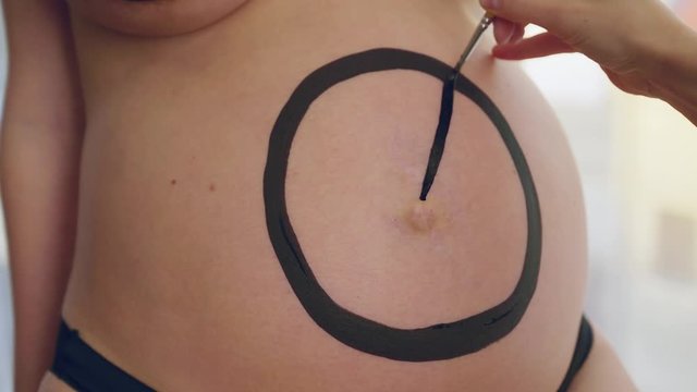 Master is performing body-art treatments in art studio. Woman is decorating pregnant belly of client woman