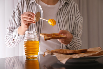 Woman pouring honey onto toast at black table, closeup