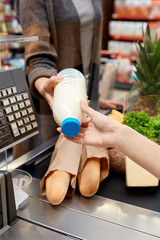 Daily Shopping. Woman standing at checkout counter while cashier checking out bottle of milk close-up