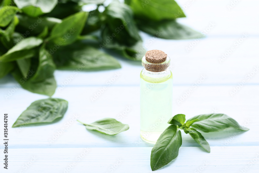 Wall mural bottle of essential oil with basil leafs on wooden table